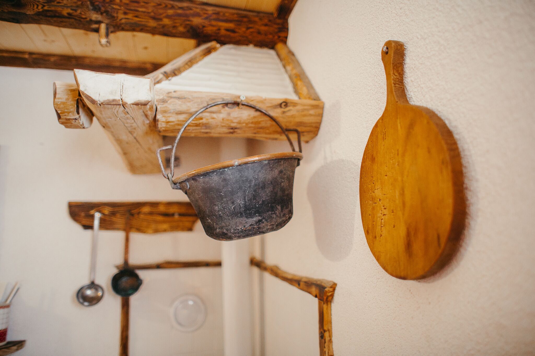 A rustic kitchen with wooden utensils and a metal bucket hanging on a wooden rack.