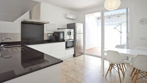 A modern kitchen with a central island, built-in oven, microwave, and refrigerator. There is a dining area with a table and chairs.