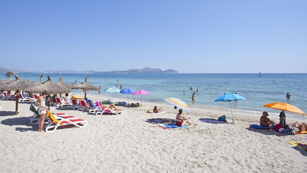 A beach with sun loungers and umbrellas, clear skies, and calm sea.