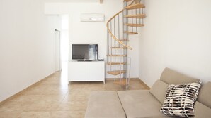 A modern living room with a spiral staircase, a flat-screen TV, a sofa, and a patterned pillow.
