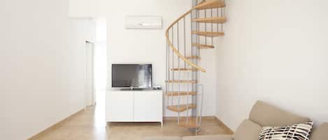 A modern living room with a spiral staircase, a flat-screen TV, a sofa, and a patterned pillow.