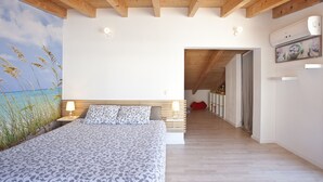 A bedroom with a large bed, wooden beams, a view of the sea, and a hallway leading to another room.