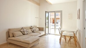 A modern living room with a sofa, a dining table, and a sliding glass door leading to an outdoor area.