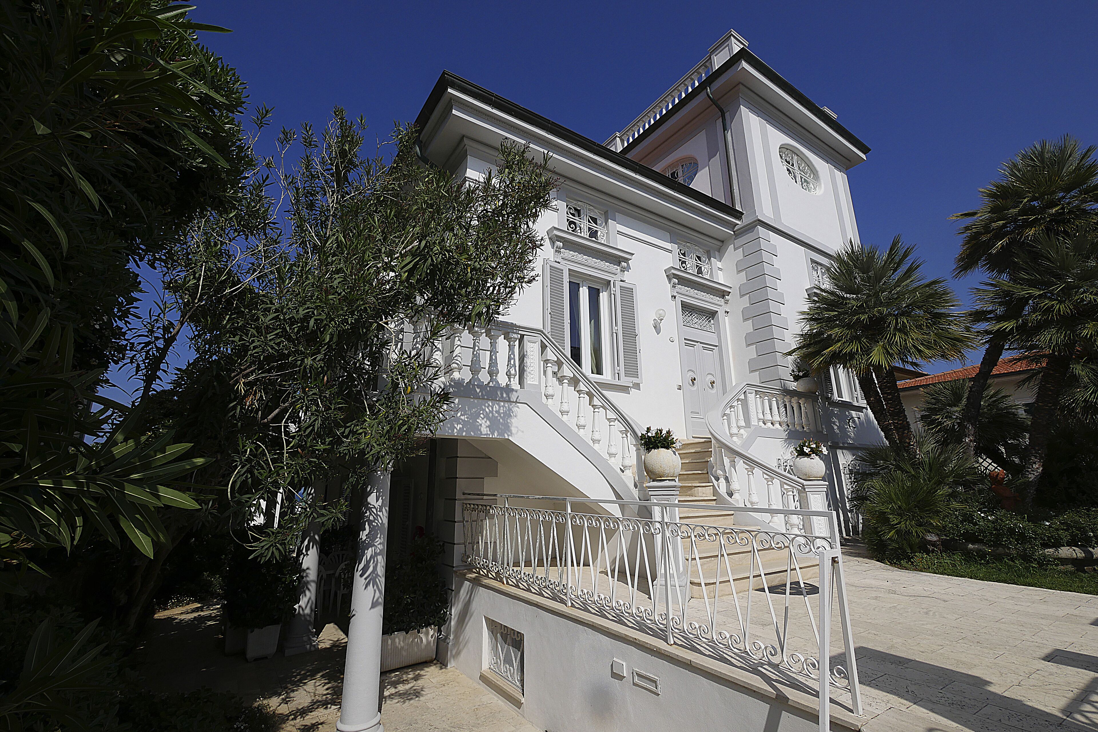 A white building with a clock tower, a staircase, and a balcony.