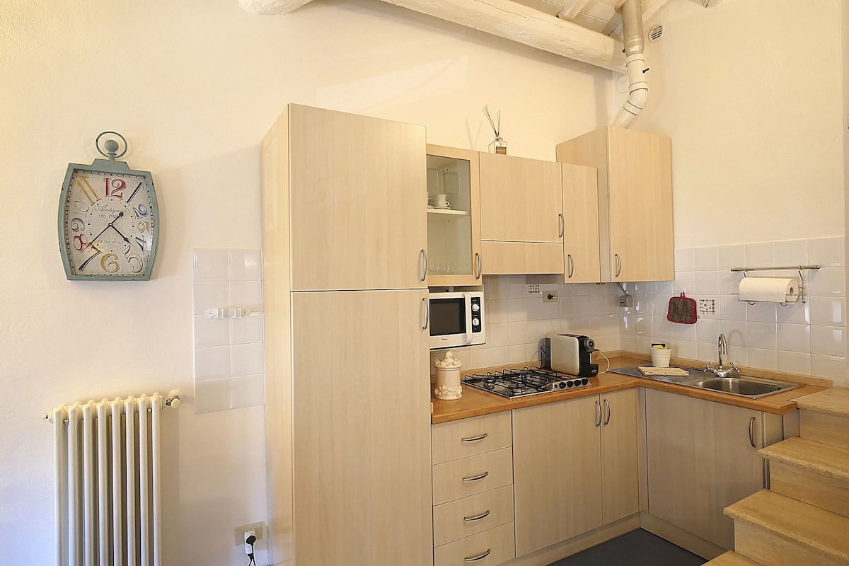 A kitchen with light wood cabinets, a microwave, a gas stove, and a wall clock.