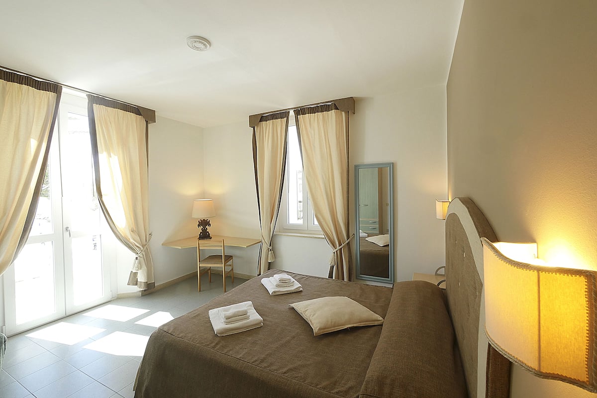A hotel room with a bed, a desk, a chair, and a mirror.