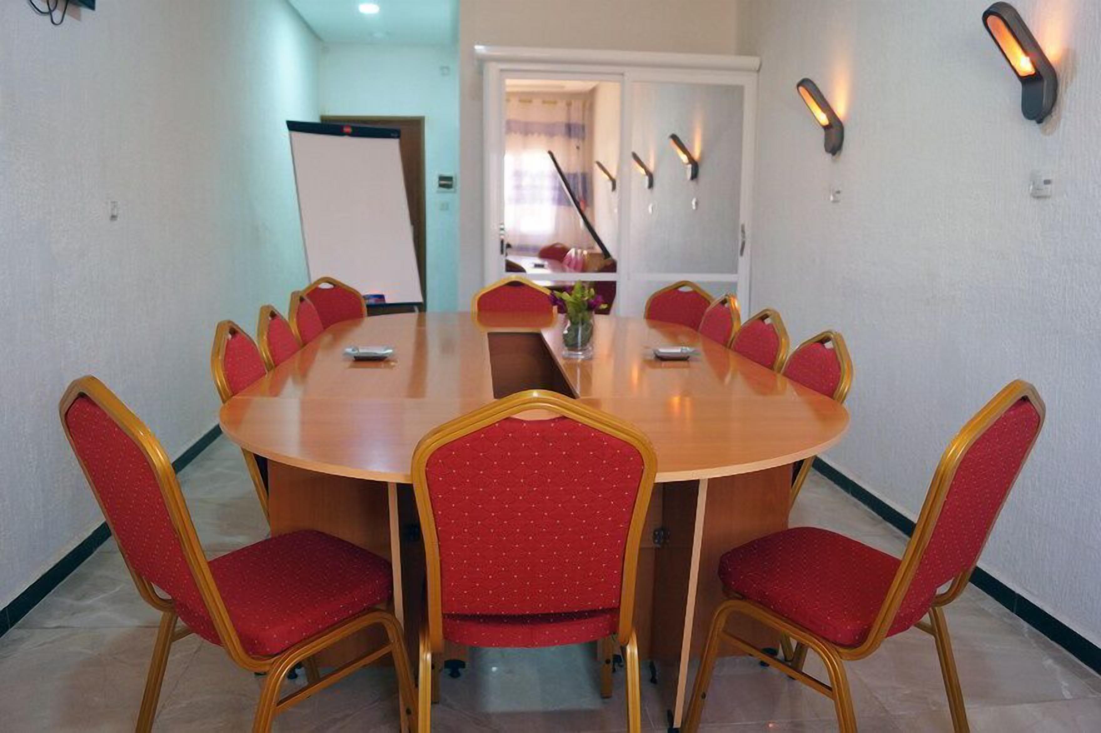 Une salle de conférence équipée d’une table ronde, de chaises rembourrées en tissu rouge et d’un tableau blanc.