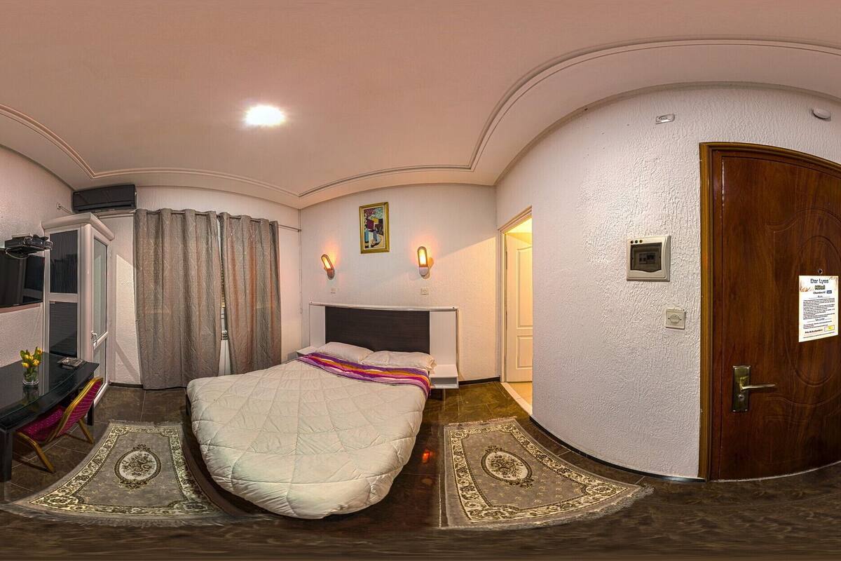A hotel room with a bed, a desk with a chair, a television, and a door with a sign.