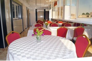 Un comedor con mesas redondas, sillas tapizadas en rojo y mantel a cuadros.