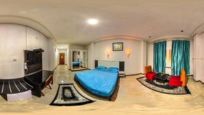 Habitación de hotel con cama, televisión, escritorio y zona de estar con mesa y sillas.