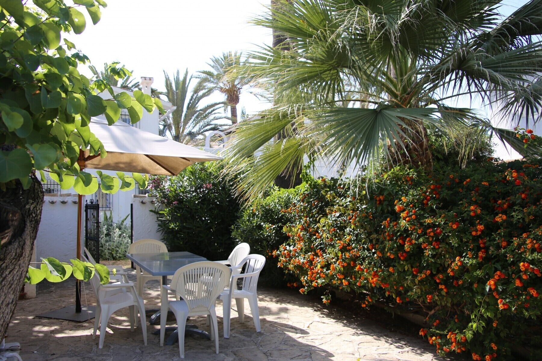 Eine Terrasse im Freien mit Tisch und Stühlen, umgeben von üppiger Bepflanzung und blühenden Pflanzen.