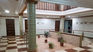 A spacious lobby with a checkered floor, large columns, potted plants, and a staircase. - Medrie International Hotel (Freetown)