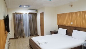A hotel room with a bed, curtains, a TV, and an air conditioning unit. - Medrie International Hotel (Freetown)
