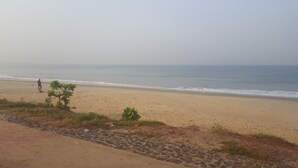 A beach with a person standing near the water, a clear sky, and a rocky path leading to the beach. - Medrie International Hotel (Freetown)