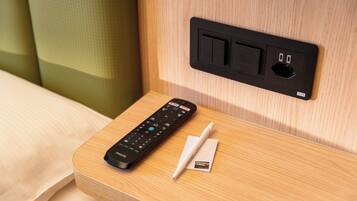 Un control remoto y un bolígrafo sobre una mesita de noche de madera con un enchufe y puertos USB.