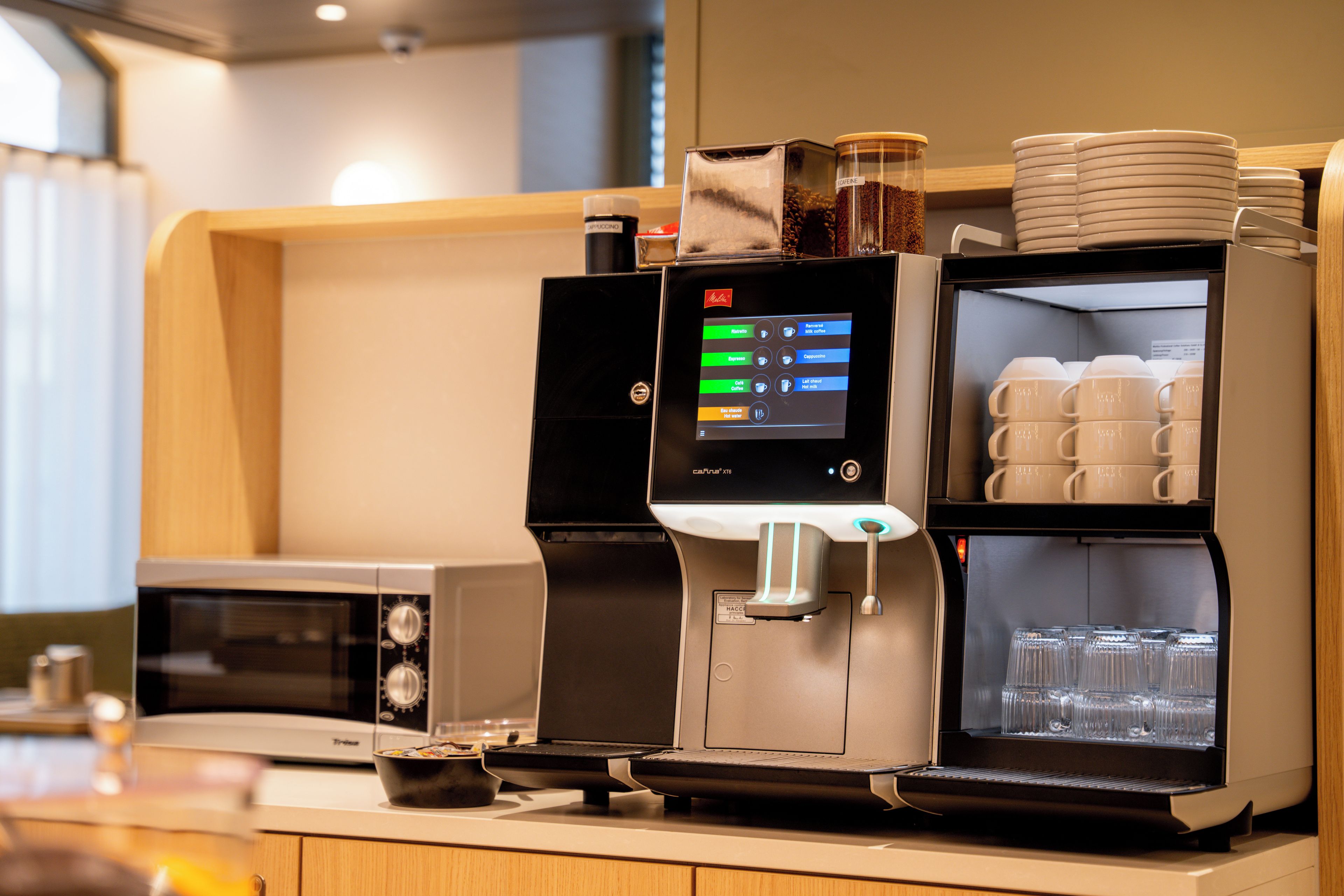 Eine Kaffeemaschine mit Digitalanzeige, eine Kaffeemühle und ein Milchaufschäumer.