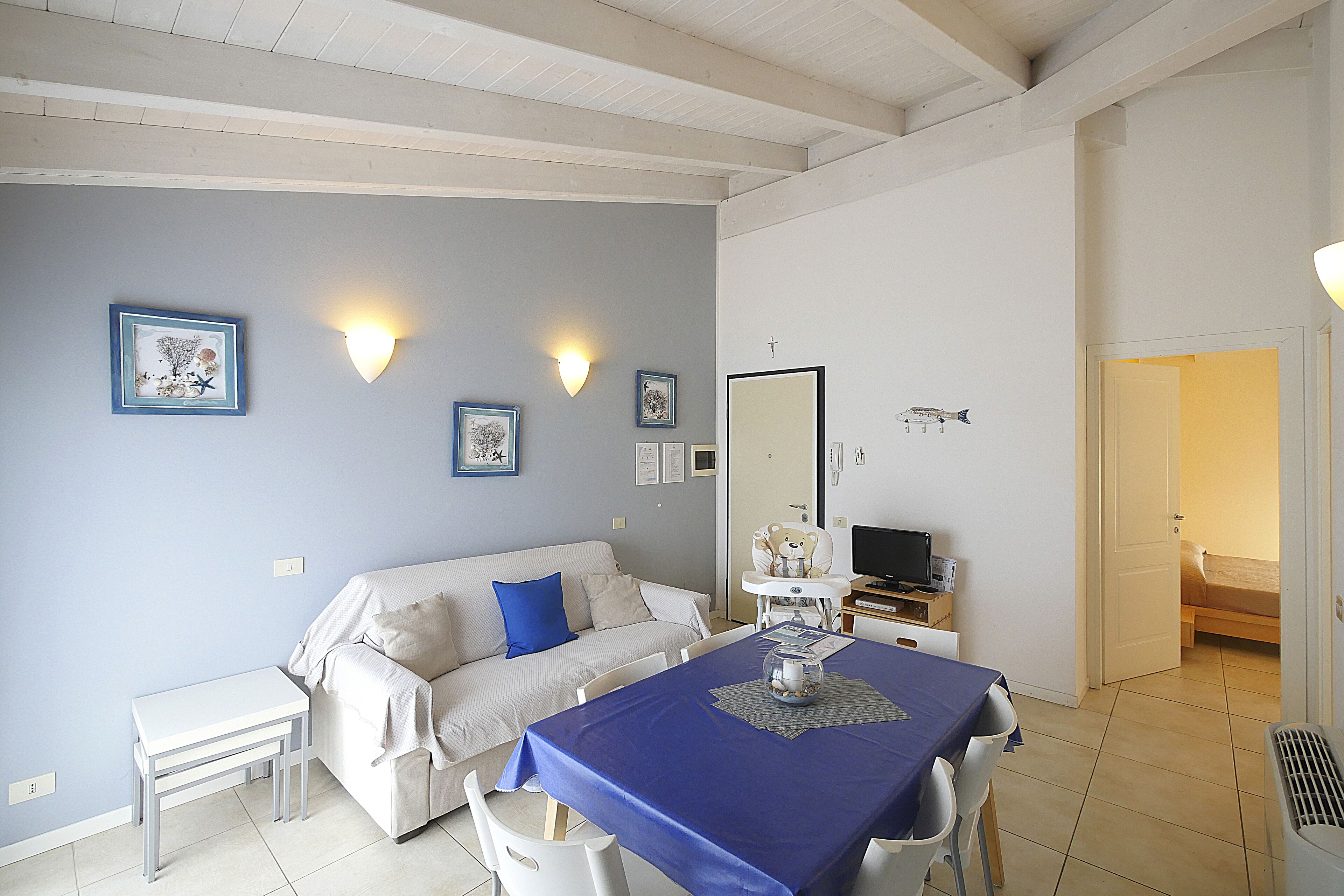 A room with a sofa, a dining table with chairs, a TV, and a bed.