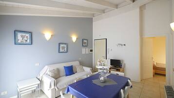A room with a sofa, a dining table with chairs, a TV, and a bed.