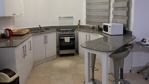 A compact kitchen with white cabinets, a gas stove, a microwave, and a window with blinds. - One bedroom (403) touristic area, near to Mamsha Street (Hurghada)