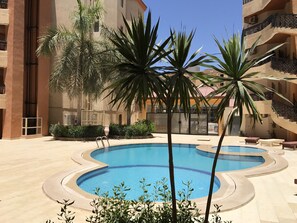 Una piscina de diseño curvo, rodeada de palmeras y un edificio con balcones.