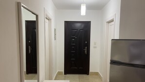 A hallway with a black door, a white bench, and a refrigerator. - One bedroom (403) touristic area, near to Mamsha Street (Hurghada)