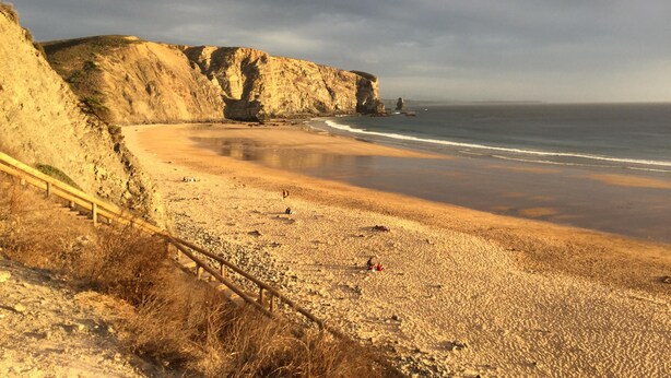 Una playa costera con acantilados, una orilla arenosa y una barandilla.