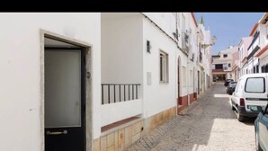 Una estrecha calle adoquinada flanqueada por edificios blancos, una puerta negra y coches estacionados.