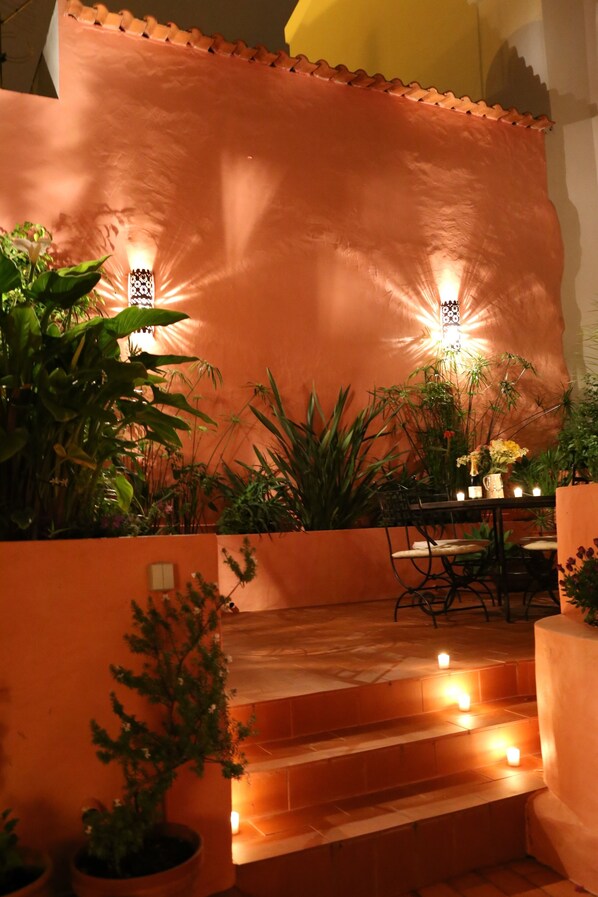 A cozy indoor garden with a table and chairs, surrounded by potted plants and warm lighting. - Unique Garden Apartment in the Heart of Lagos Old City (Lagos)
