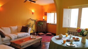 Una sala de estar con sofá, mesa de centro y comedor con mesa dispuesta para el desayuno.