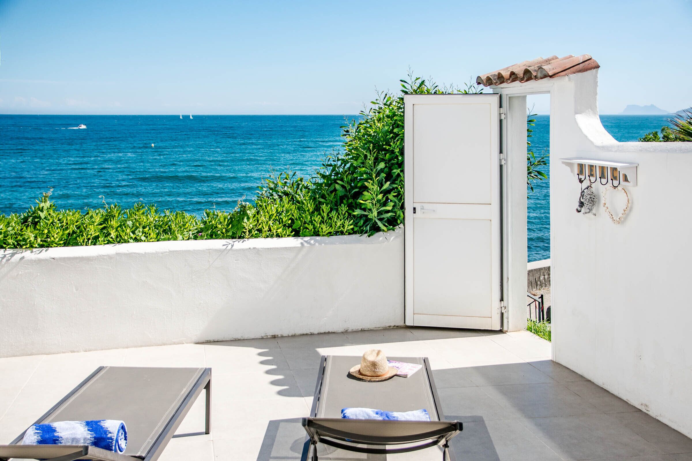 Un balcon avec deux chaises longues, une porte donnant sur une terrasse et une vue sur la mer.