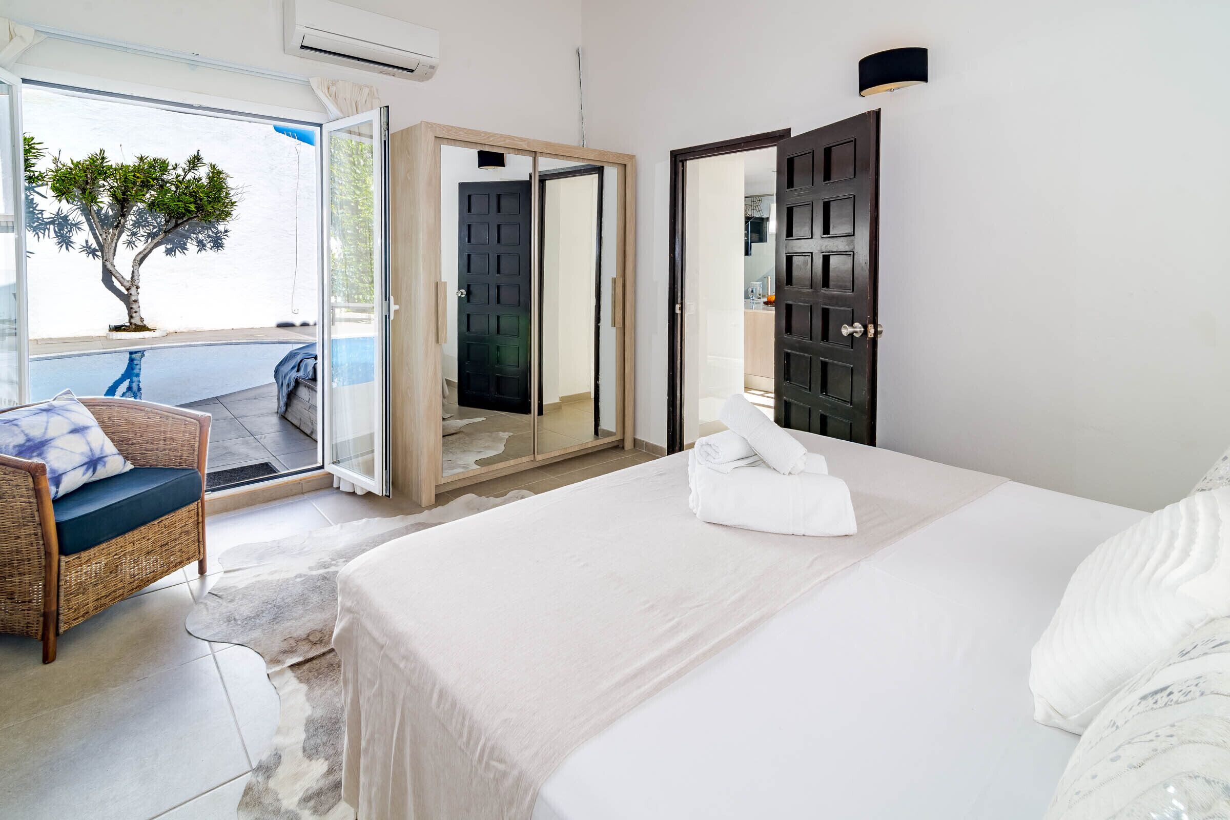 Een slaapkamer met een bed, een stoel, een tafeltje en uitzicht op buiten.