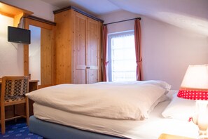 Ein Schlafzimmer mit Bett, Sessel, Kleiderschrank, Fernseher und einem Fenster mit Vorhängen.