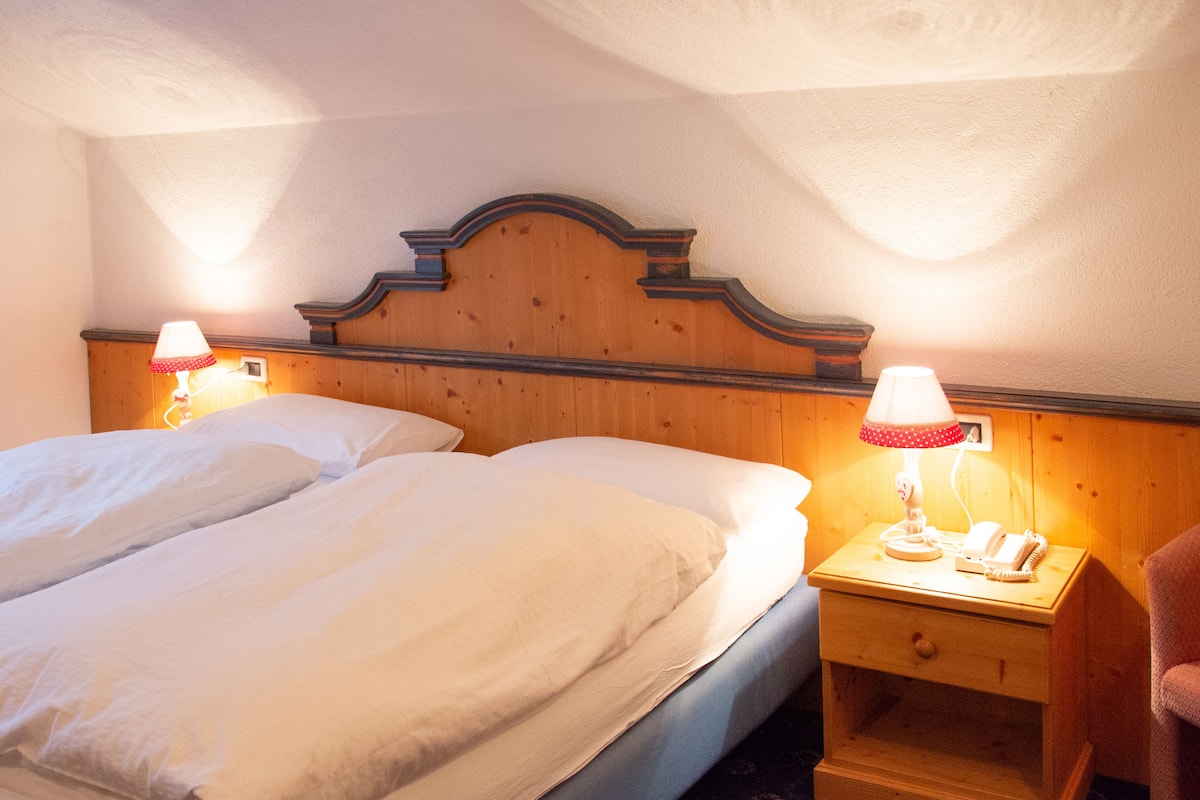 Ein Hotelzimmer mit zwei Betten, einem Holz-Kopfteil, Nachttischlampen und einem kleinen Nachttisch mit Lampe.