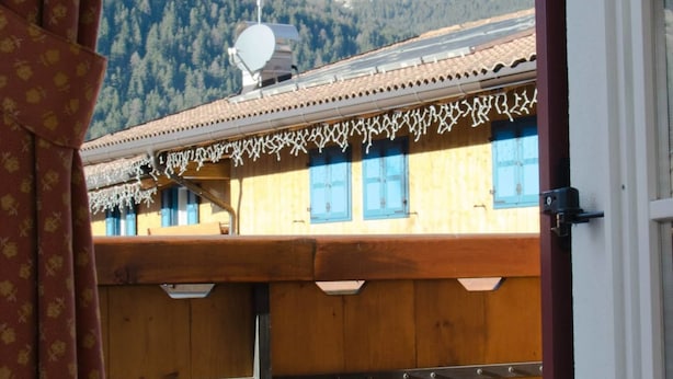 Une vue sur une montagne, aperçue à travers une fenêtre, avec un bâtiment en bois au premier plan.