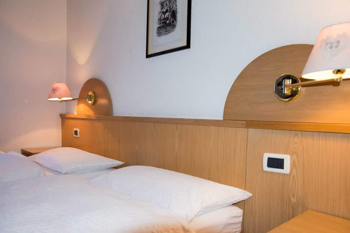 Ein Hotelzimmer mit einem hölzernen Kopfteil, zwei Betten mit weißen Laken, einer Wandlampe und einem gerahmten Bild.
