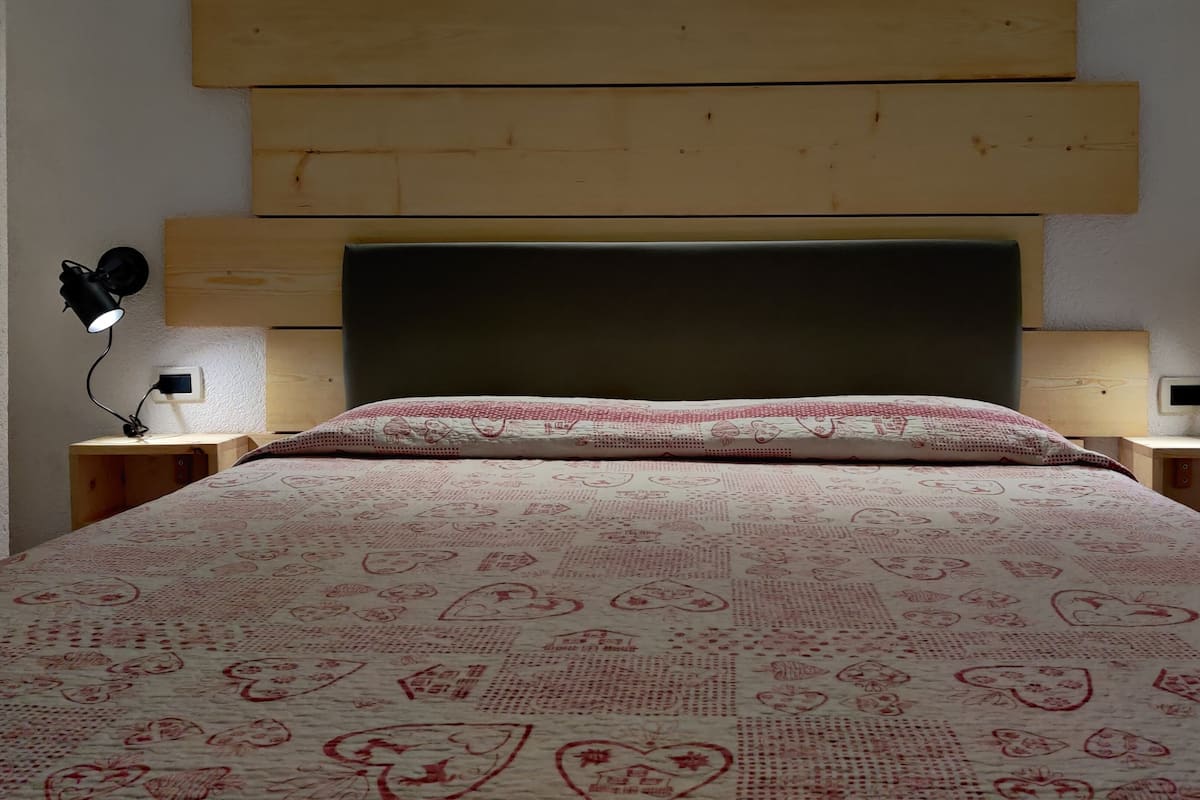 Ein Bett mit einem gemusterten Überwurf, einem Holzkopfschild und zwei Nachttischlampen.