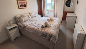 A bedroom with a bed, bedside table, lamp, window with curtains, and a mirror. - Smithy Cottage, Perthshire (Perth)