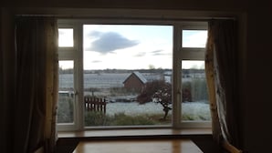 A room with a large window, a wooden table, and curtains. - Smithy Cottage, Perthshire (Perth)