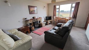 A living room with a sofa, a television, a fireplace, and a dining area with a table and chairs. - Smithy Cottage, Perthshire (Perth)