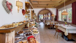 A restaurant with a long counter filled with various pastries and desserts, wooden furniture, and large windows providing natural light. - Small & Lovely Hotel Zaluna (Predazzo)