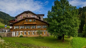 A two-story wooden building with a stone facade, a balcony with flowers, and a sign indicating a restaurant. - Small & Lovely Hotel Zaluna (Predazzo)