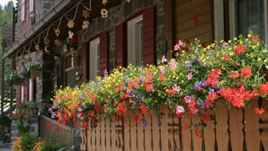 A wooden building with a balcony adorned with colorful flowers and a wooden fence. - Small & Lovely Hotel Zaluna (Predazzo)