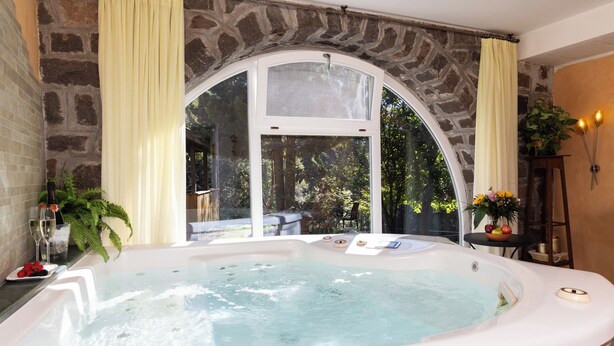 A spa room with a hot tub, stone walls, and a view of greenery outside. - Small & Lovely Hotel Zaluna (Predazzo)