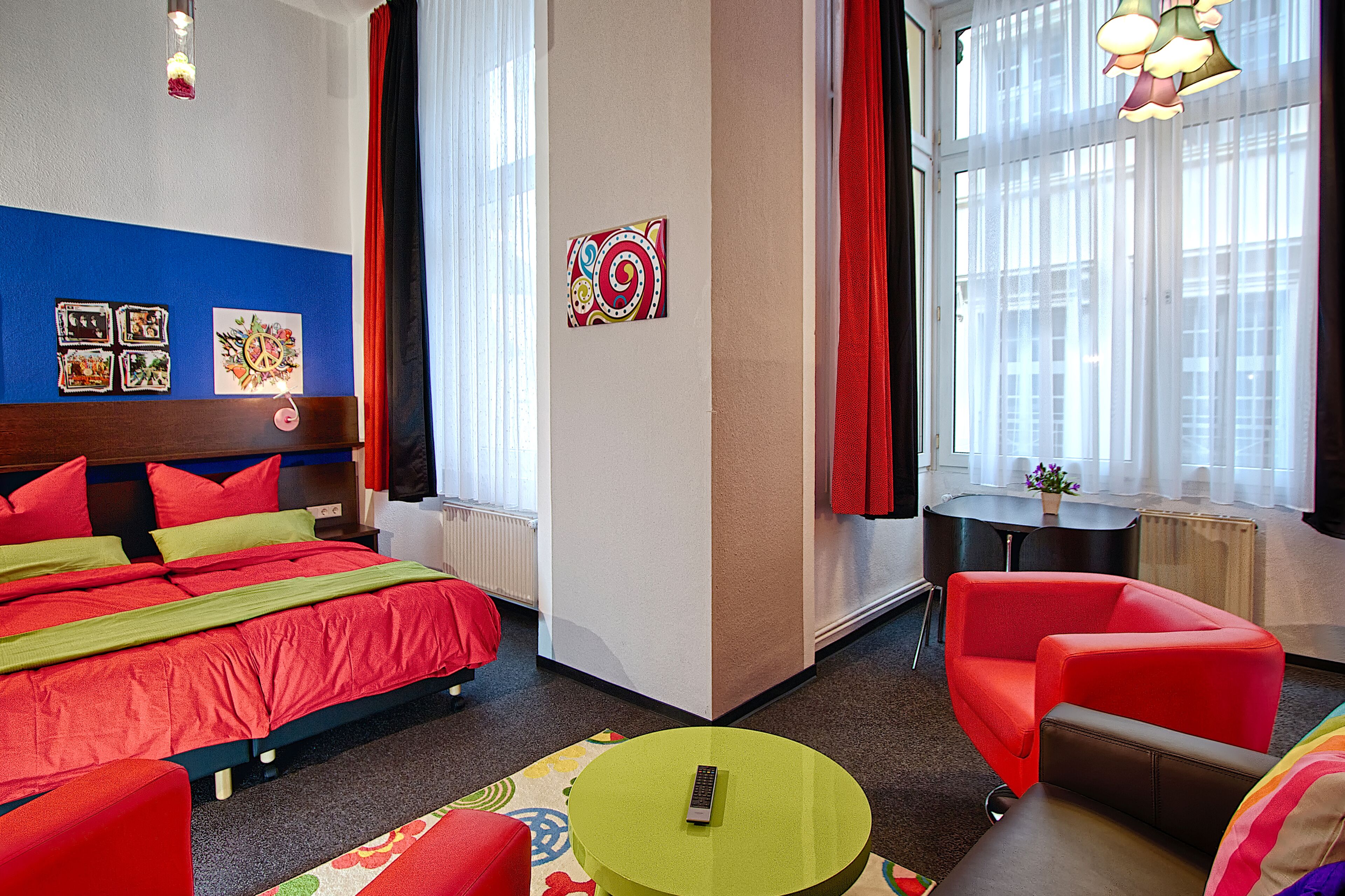 A hotel room with a bed, a green table, a red sofa, and a window with curtains.