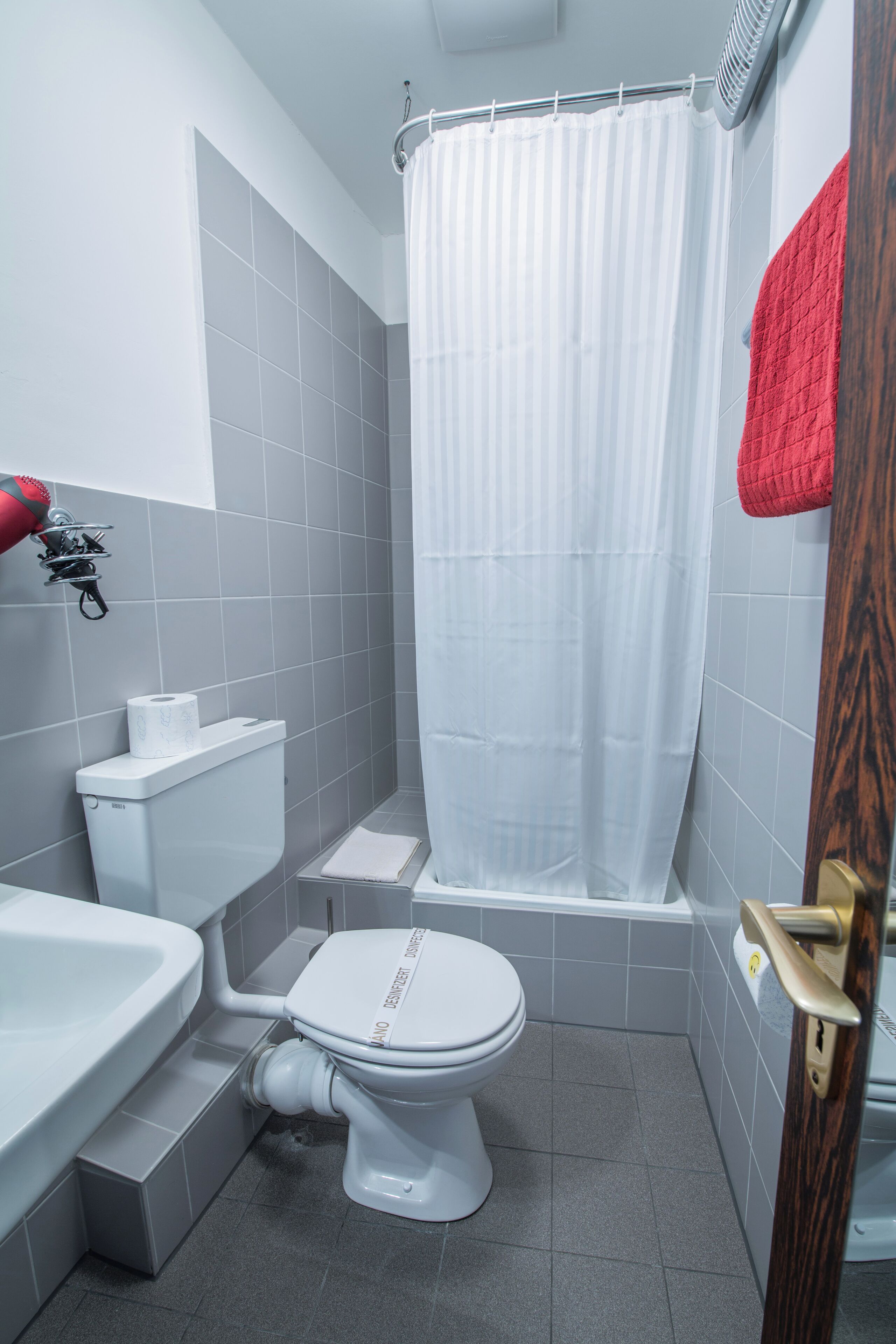 A bathroom with a white toilet, a shower curtain, and a red towel hanging on the wall.