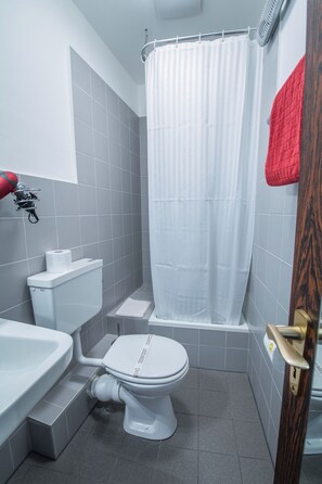 Un baño con inodoro blanco, cortina de ducha y una toalla roja colgada en la pared.