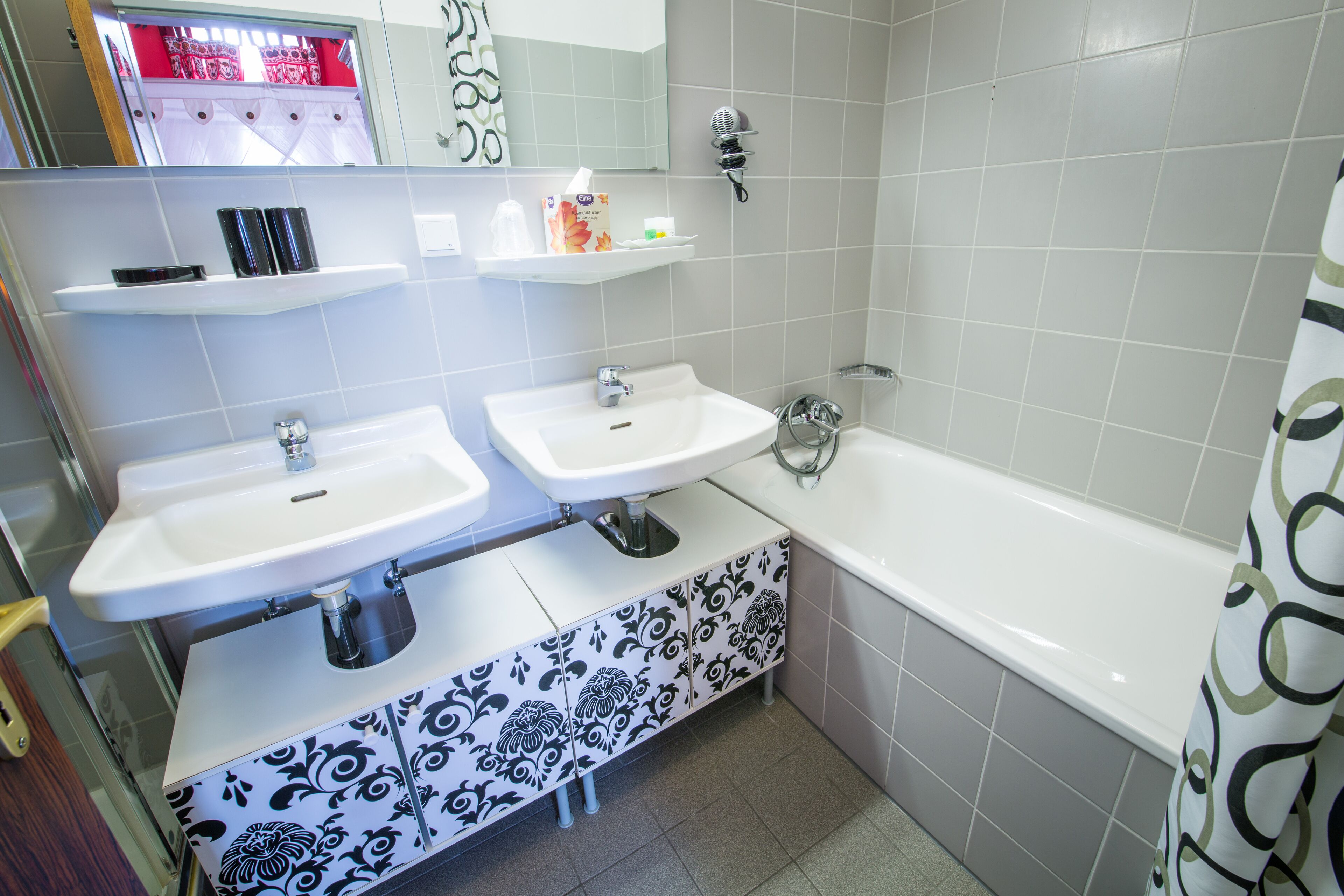 A bathroom with two sinks, a mirror, a shelf with toiletries, and a bathtub.