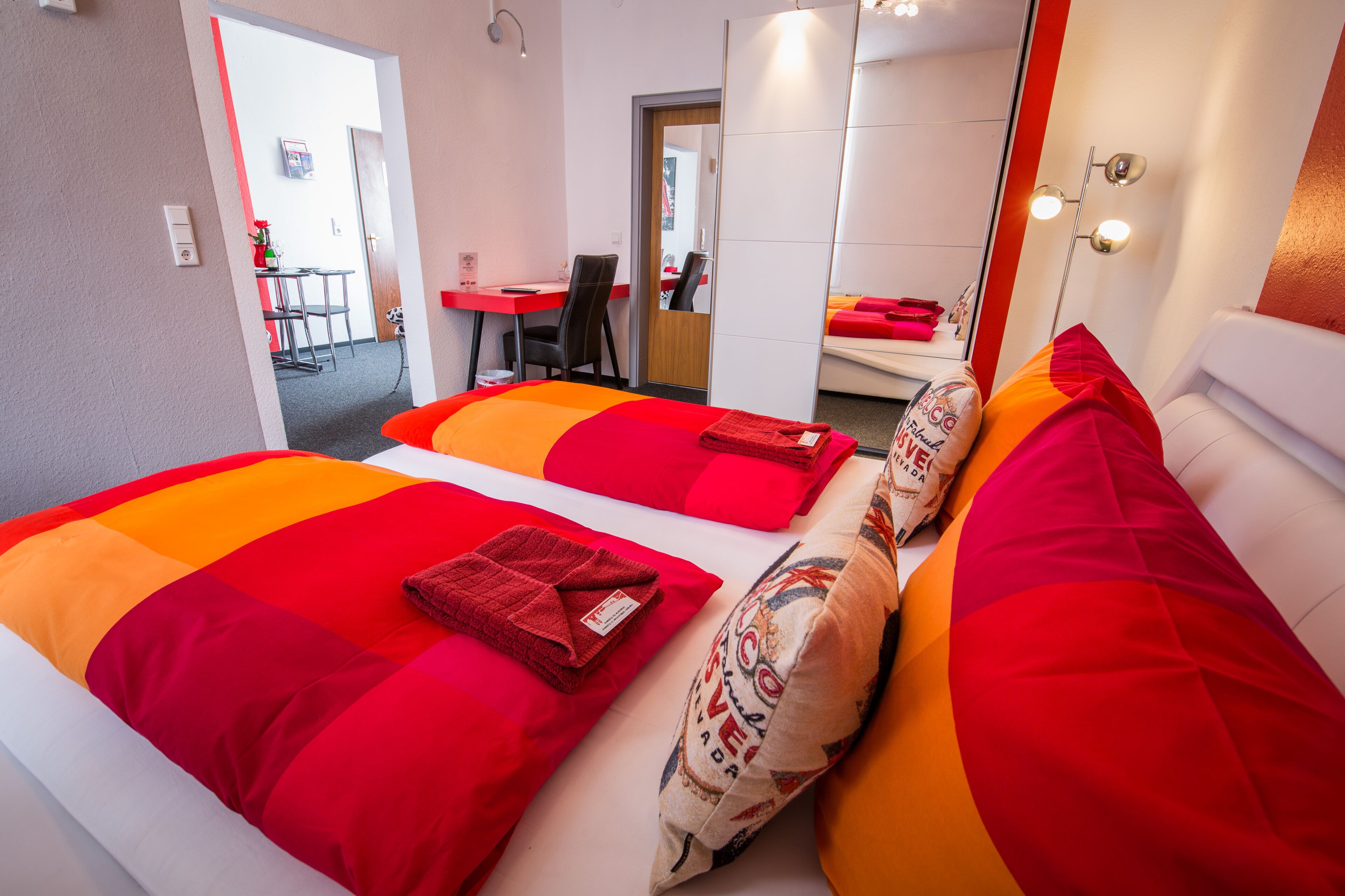 Habitación de hotel con dos camas, cada una con ropa de cama rojo anaranjada, un escritorio y una silla.