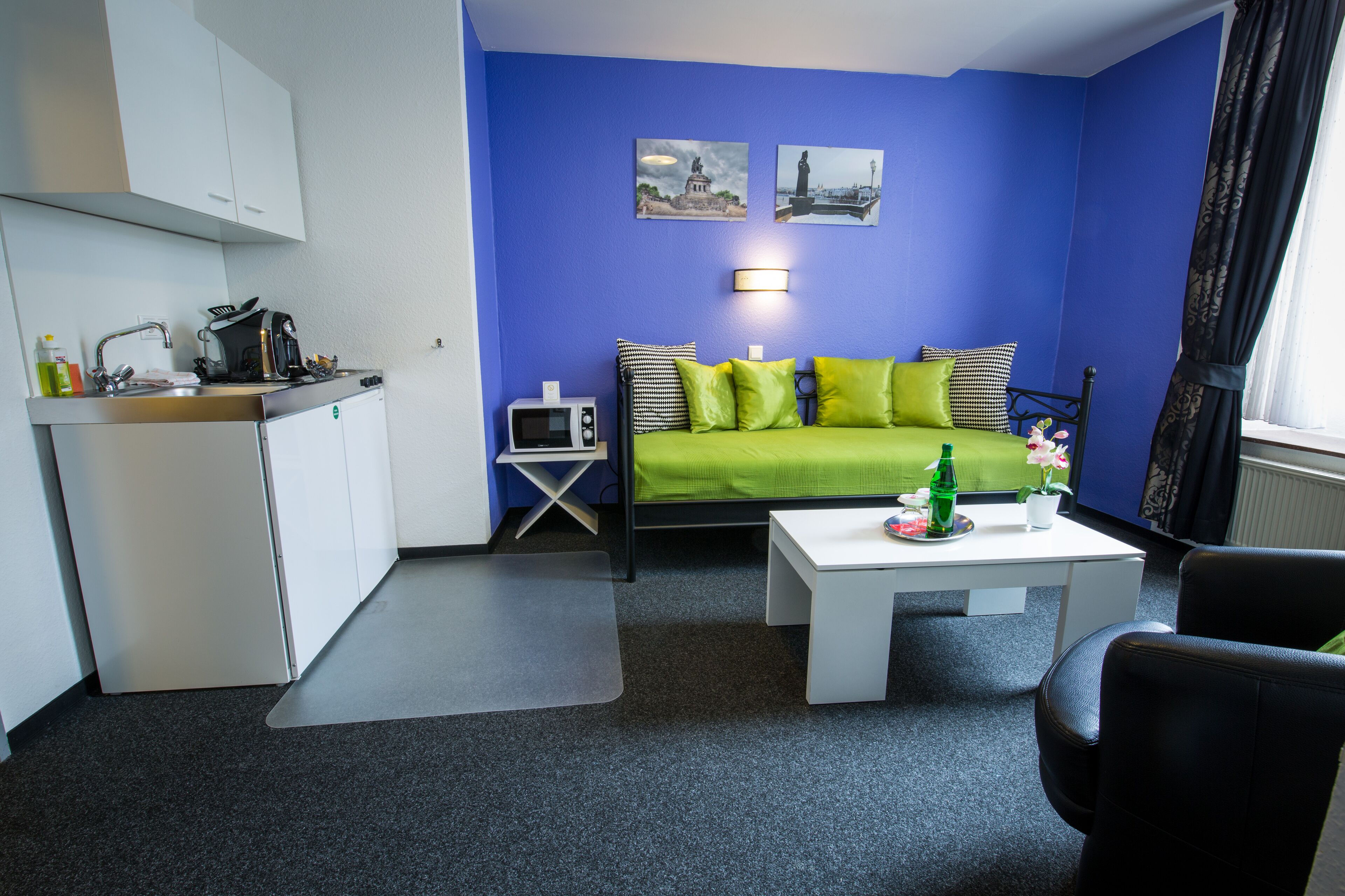 Une pièce compacte comprenant un coin cuisine, un canapé vert, une petite table et une chaise noire.
