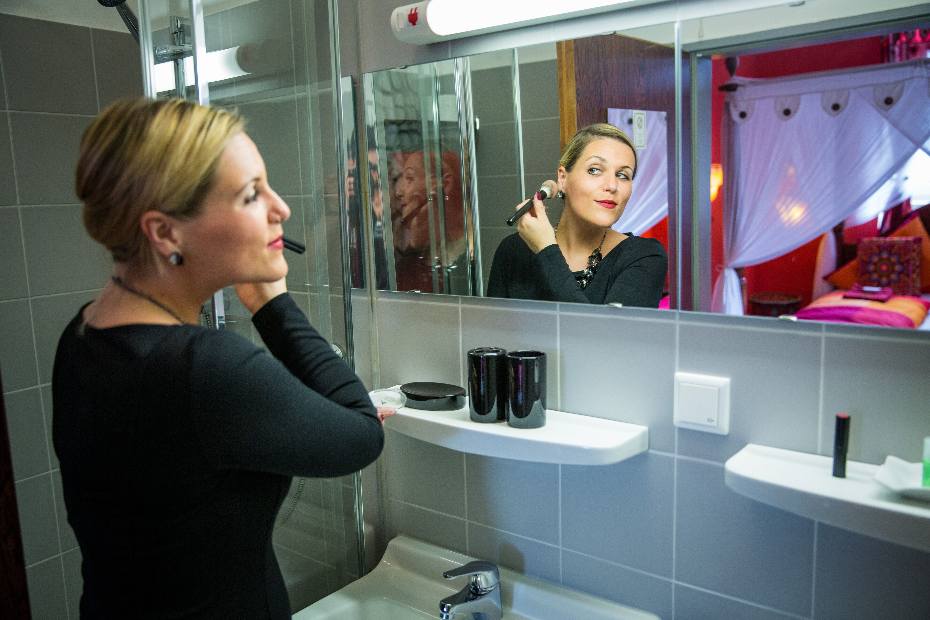 A bathroom with a mirror, a sink, and a shelf with toiletries.